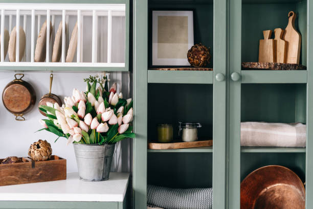 Cuisine de couleur verte avec portes de placard en verre et sur le plan de travail un gros bouquet de tulipes rose pâle et rose fuchsia à la base dans un sceau en zinc
